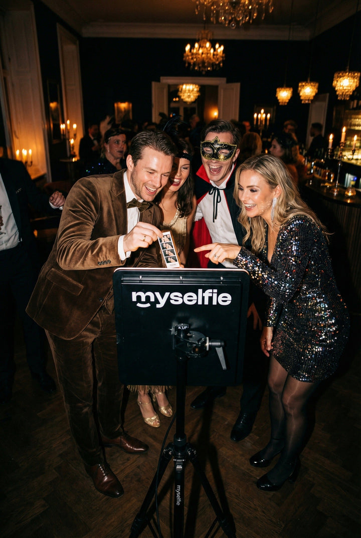 Gäster i festkläder och masker skrattar och tar bilder vid Myselfie fotobås på en temafest