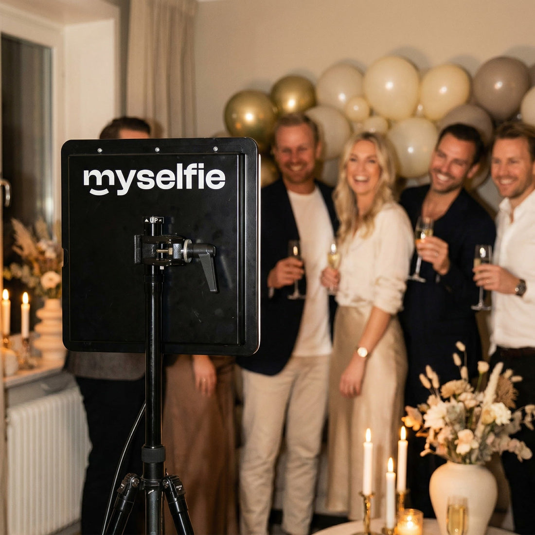Gäster med champagne framför Myselfie fotobås och guldballonger på en födelsedagsfest