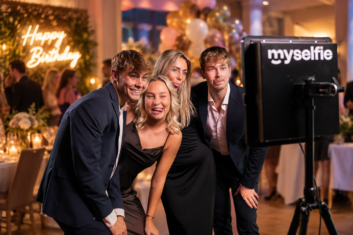 Unga vänner skrattar framför Myselfie fotobås och en Happy Birthday-skylt